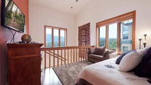 A bedroom with a large bed, a wooden desk, a view of a forest through a window, and a balcony with a railing. - Pet Friendly Home at Purgatory - Decks with Amazing Views - Steps to Lifts (Durango)