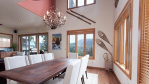 A spacious dining area with a wooden table and white chairs, large windows with mountain views, and a decorative chandelier. - Pet Friendly Home at Purgatory - Decks with Amazing Views - Steps to Lifts (Durango)