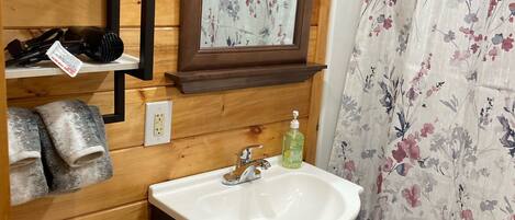 Un baño con tocador de madera, un lavamanos, inodoro y cortina de ducha.