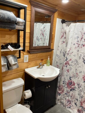 A bathroom with a wooden vanity, a sink, a toilet, and a shower curtain. - Tiny house, loft bedroom, near the river, Cooperstown and Baseball hall of fame (Richfield Springs)