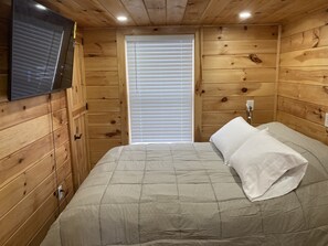 A wooden-paneled room with a bed, a television mounted on the wall, and a window with blinds. - Tiny house, loft bedroom, near the river, Cooperstown and Baseball hall of fame (Richfield Springs)