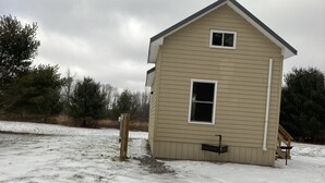 A single-story, beige wooden house with a small porch and a window. - Tiny house, loft bedroom, near the river, Cooperstown and Baseball hall of fame (Richfield Springs)
