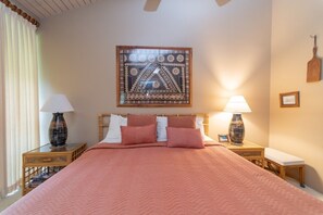 Una cama bien tendida con un edredón rosa, dos mesitas de noche con lámparas, un cabecero de madera y una obra de arte colgada en la pared.