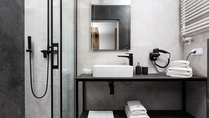A modern bathroom with a glass shower enclosure, a black vanity with a white sink, and neatly folded towels. - Wooden Studio/ Aircon/ Balcony/ City Center (Kraków-Śródmieście)
