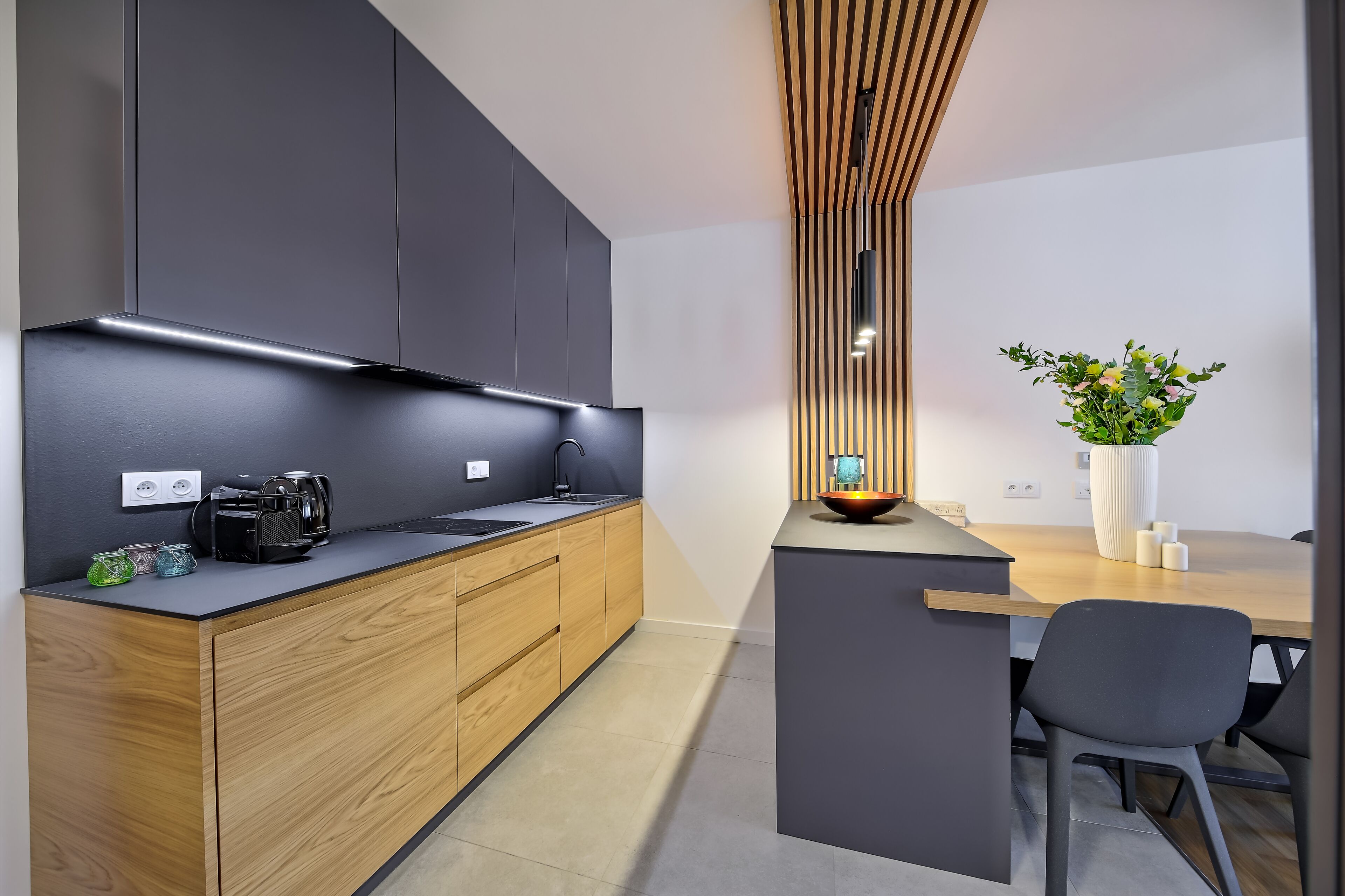 Una cocina moderna con un mueble de madera, una encimera negra y una cafetera integrada.