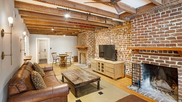 A cozy living room with a brick fireplace, leather sofa, wooden coffee table, and a TV on a cabinet. - Pet friendly, Historic Garden Level w/ King Bed & No Stairs by Lucky Savannah (Savannah)