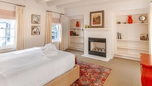 Quarto com cama, lareira, estante de livros e janela com cortinas.