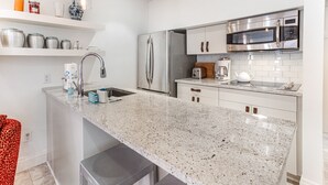 Uma cozinha moderna com bancadas de granito, eletrodomésticos de aço inoxidável e armários brancos.