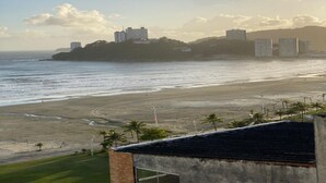 A coastal view with a beach, a building with a flat roof, and a distant cityscape. - The building is right across from the beach, and the studio apartment has a wide view of it. (SP)