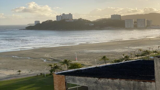 A coastal view with a beach, a building with a flat roof, and a distant cityscape. - The building is right across from the beach, and the studio apartment has a wide view of it. (SP)
