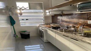 A compact kitchen with a washing machine, a stove, and a microwave. - The building is right across from the beach, and the studio apartment has a wide view of it. (SP)