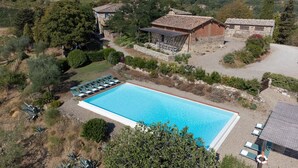 An aerial view of a property with a swimming pool, lounge chairs, and stone buildings surrounded by greenery.