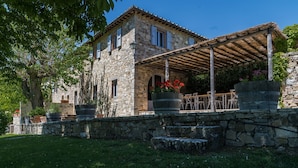 A stone building with a covered patio, stone steps, and potted plants.
