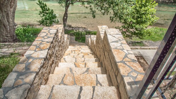 Un escalier en pierre menant à une berge bordée d’arbres et de verdure.