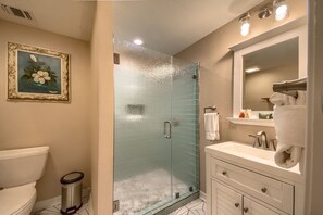 A bathroom with a glass-enclosed shower, a toilet, a sink with a mirror, and a framed painting on the wall. - Ponderosa Twins Prd 2485 5 Bedroom Home by RedAwning (New Braunfels)