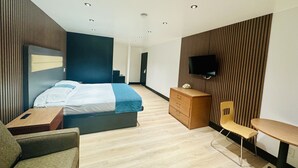 Et moderne hotelværelse med seng, skrivebord, stol, tv ophængt på væggen og træpaneler i væggene.