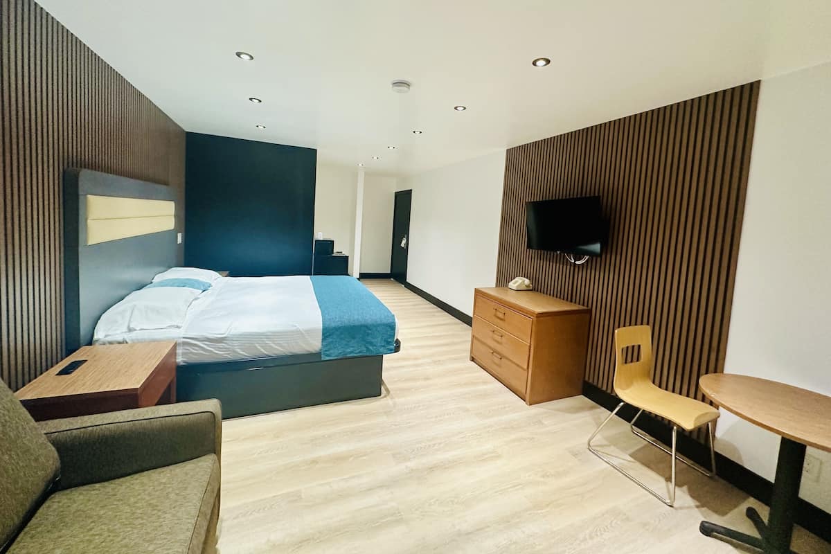 Quarto de hotel moderno com cama, escrivaninha, cadeira, televisão na parede e painéis de madeira nas paredes.