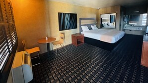 Et hotelværelse med en seng, et lille bord, en stol, et spejl og et tekøkken.