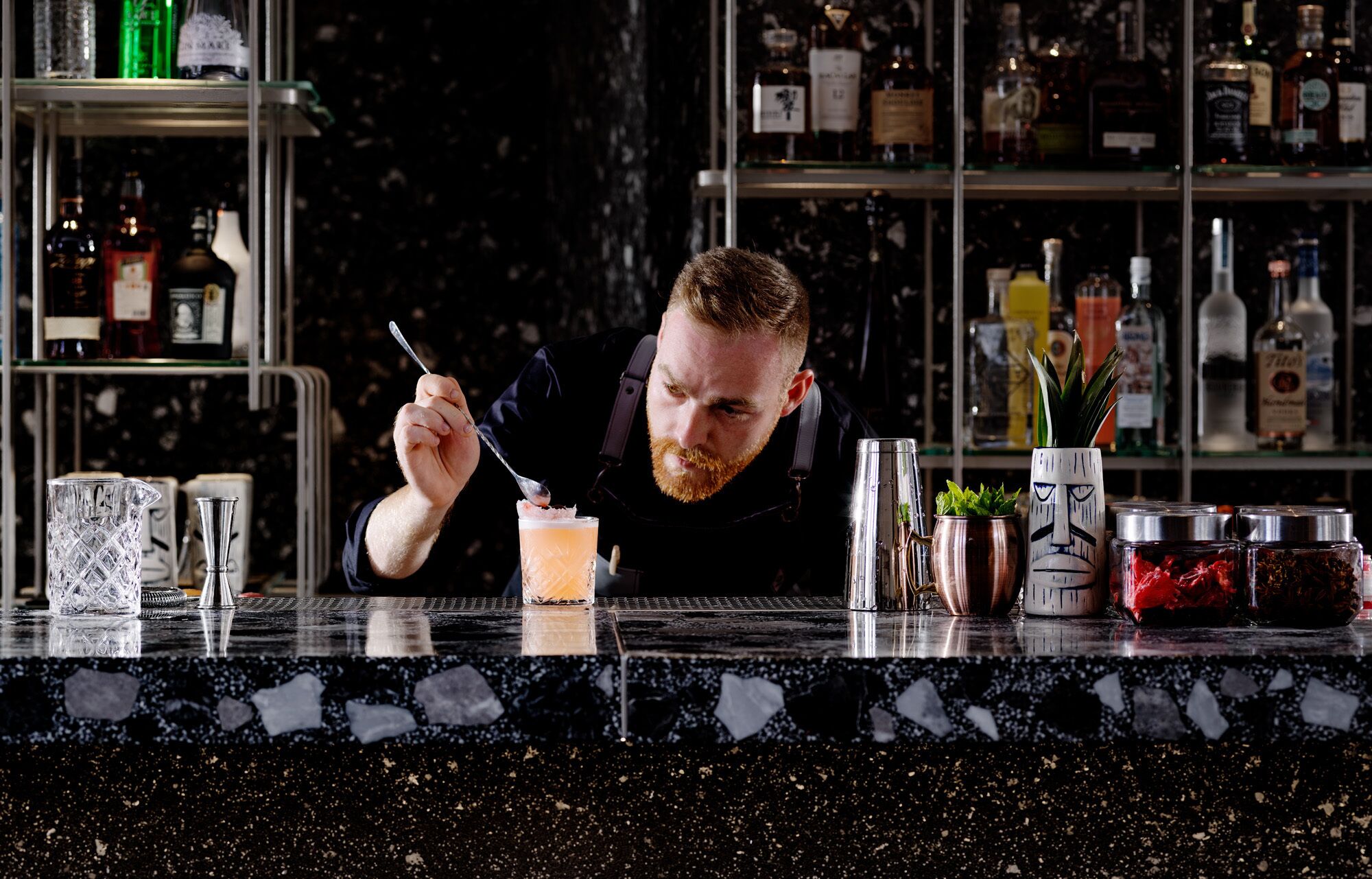 A bartender at a bar with a variety of liquor bottles in the background.