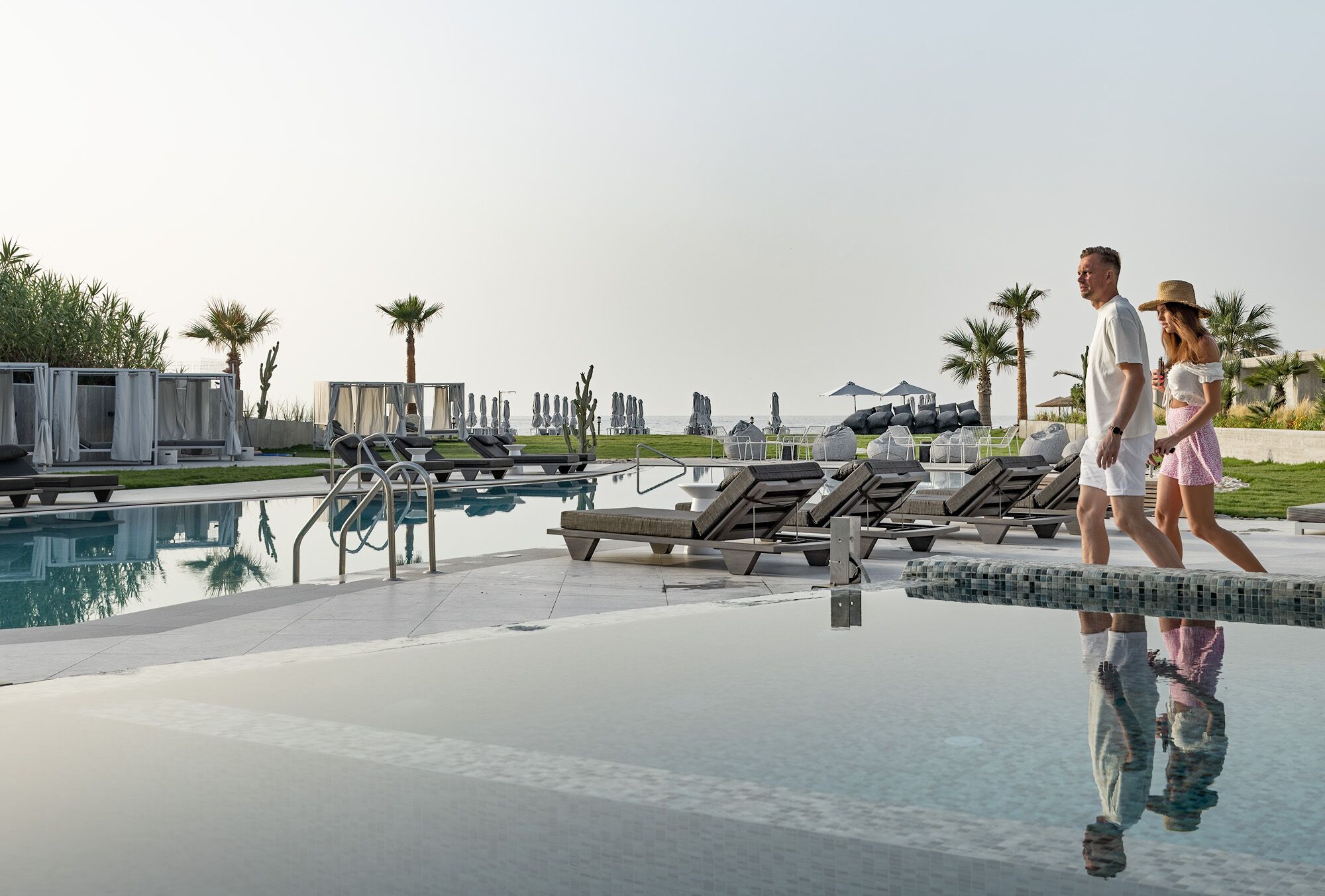 A pool area with lounge chairs, a clear pool, and palm trees.