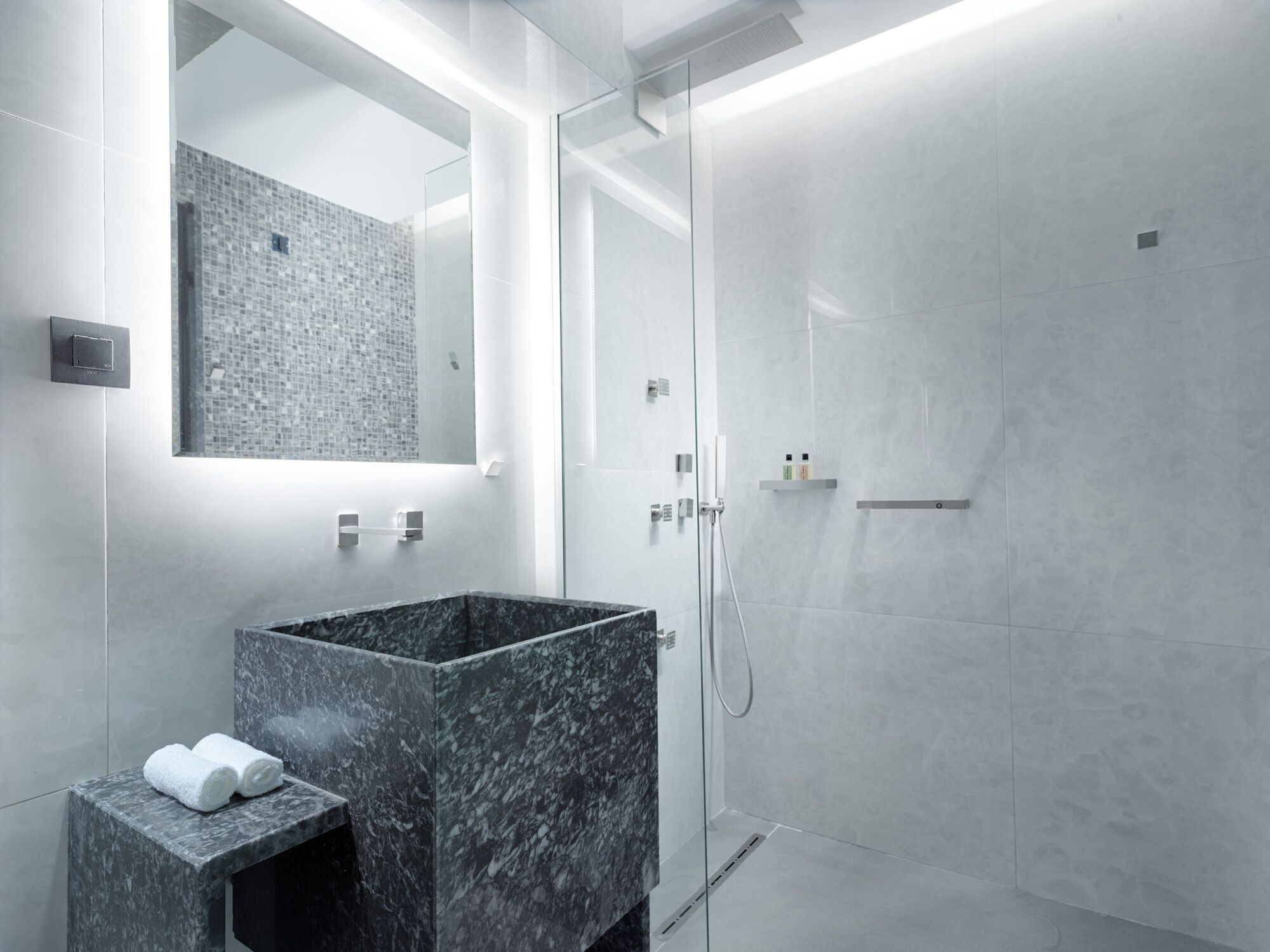 A modern bathroom with a marble sink, a glass shower enclosure, and a large mirror.