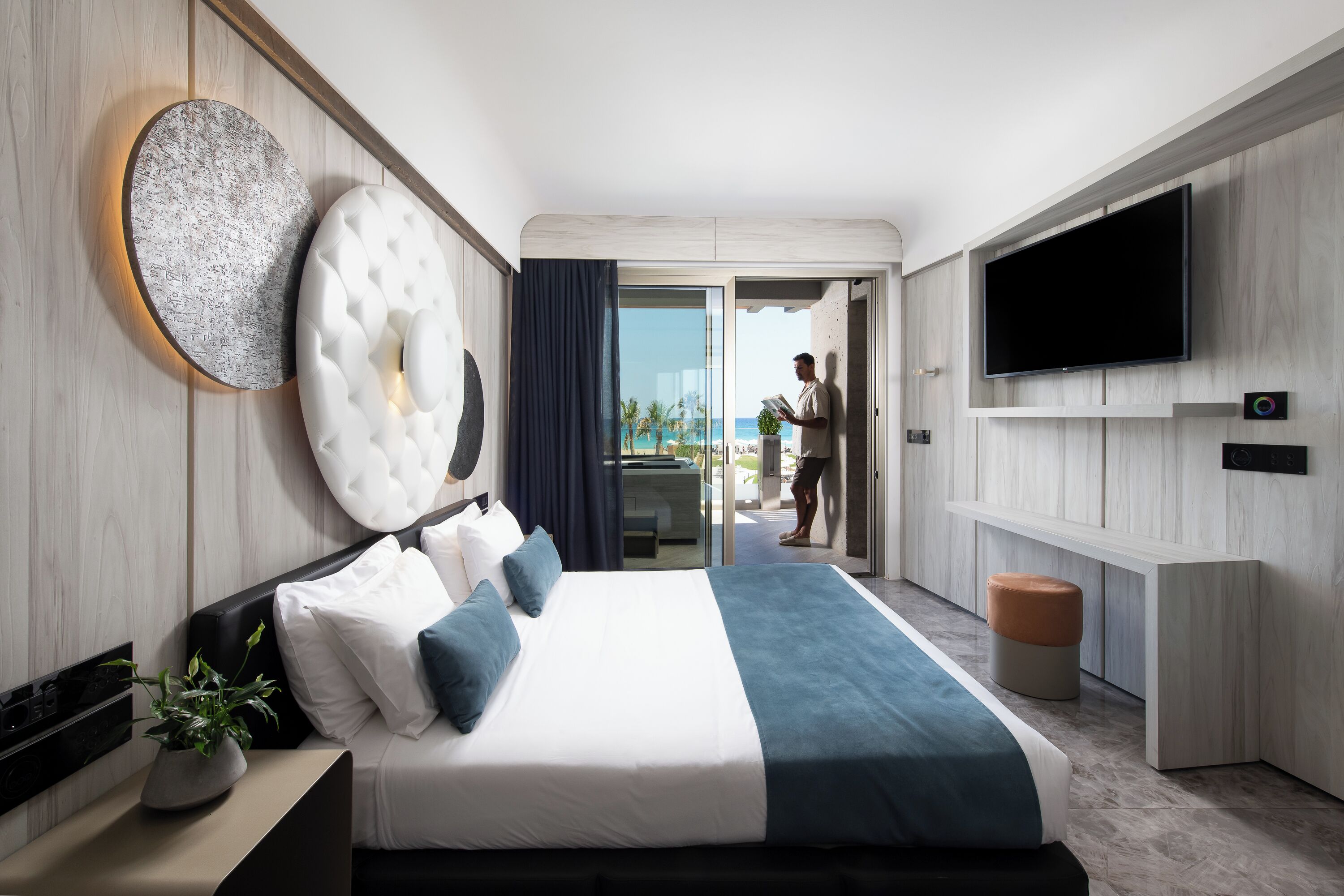 A modern hotel room with a large bed, a flat-screen TV, and a balcony with a view of the ocean.