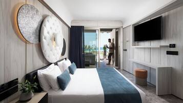 A modern hotel room with a large bed, a flat-screen TV, and a balcony with a view of the ocean.