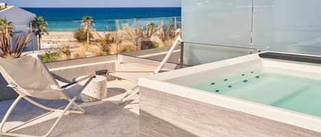 A rooftop terrace with a spa tub and lounge chairs overlooking a beach.