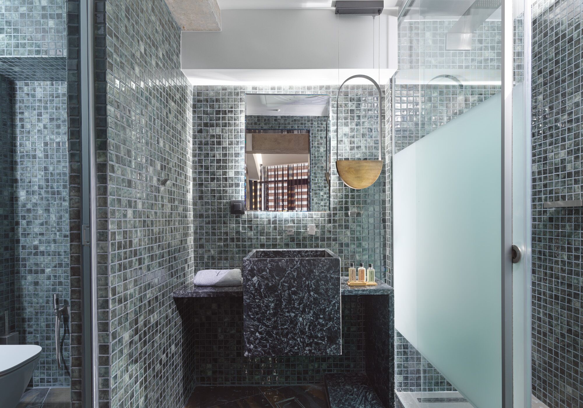 Un baño moderno con cabina de ducha de vidrio, lavamanos de mármol y pared con azulejos de vidrio.