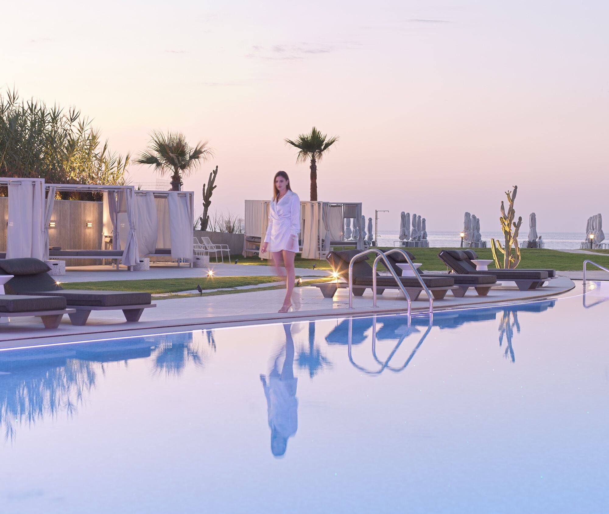 Ein Poolbereich mit Liegestühlen und Blick auf das Meer bei Sonnenuntergang.