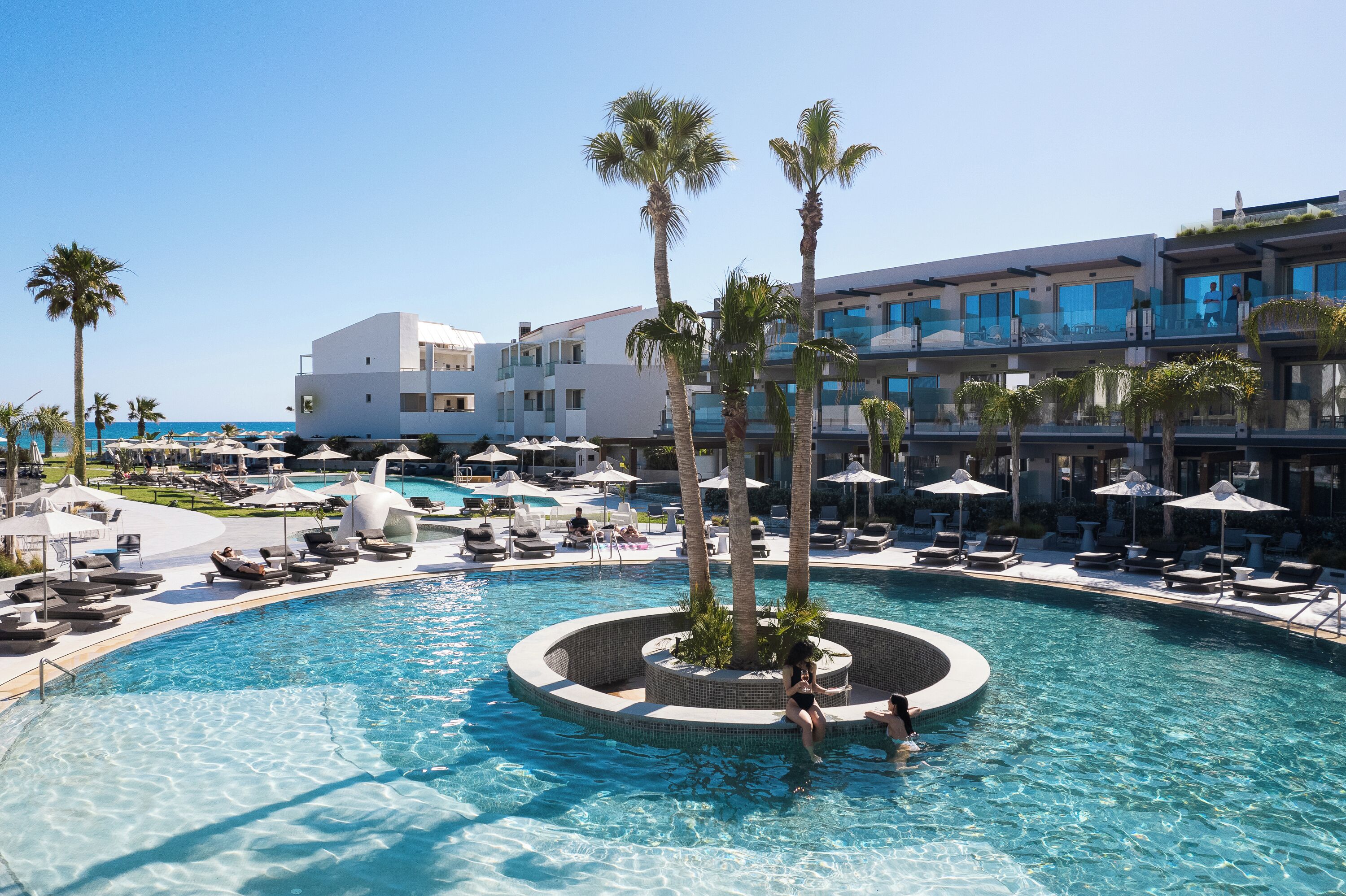 A resort pool area with lounge chairs, palm trees, and a clear view of the ocean.