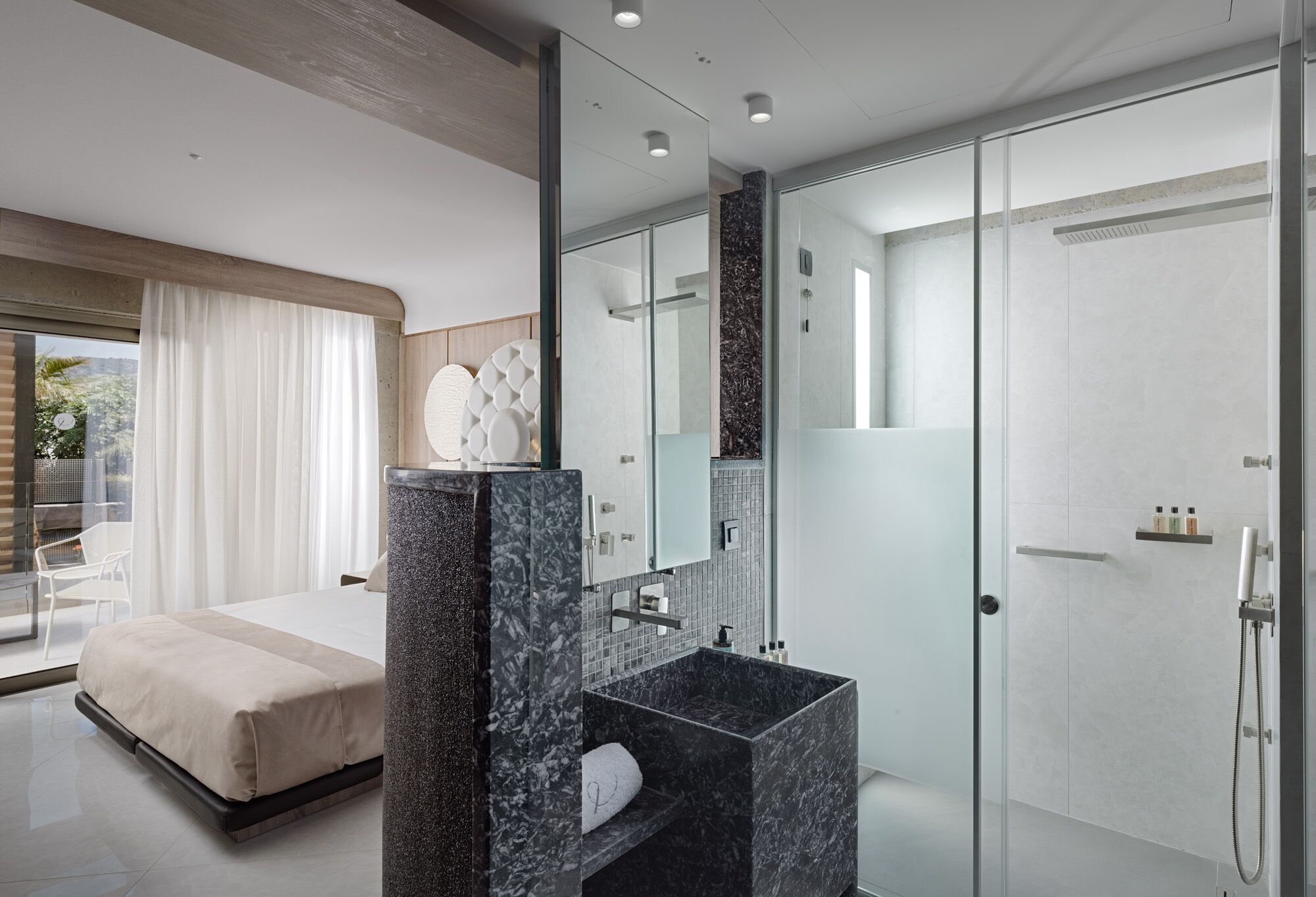 A modern hotel room with a large bed, a marble bathroom vanity, and a glass shower enclosure.