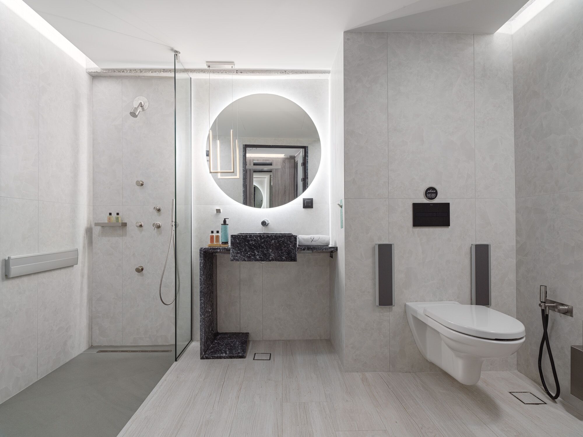 Een moderne badkamer met een douchecabine van glas, een ronde spiegel, een marmeren wastafel en een toilet.