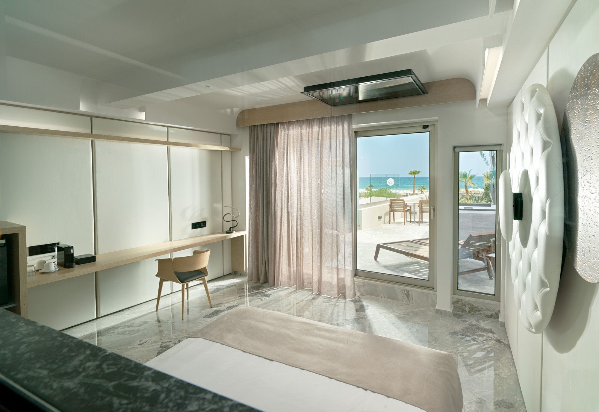 Ein modernes Hotelzimmer mit einem großen Bett, einer Sitzecke mit Blick auf den Strand und einer Glastür zum Balkon.