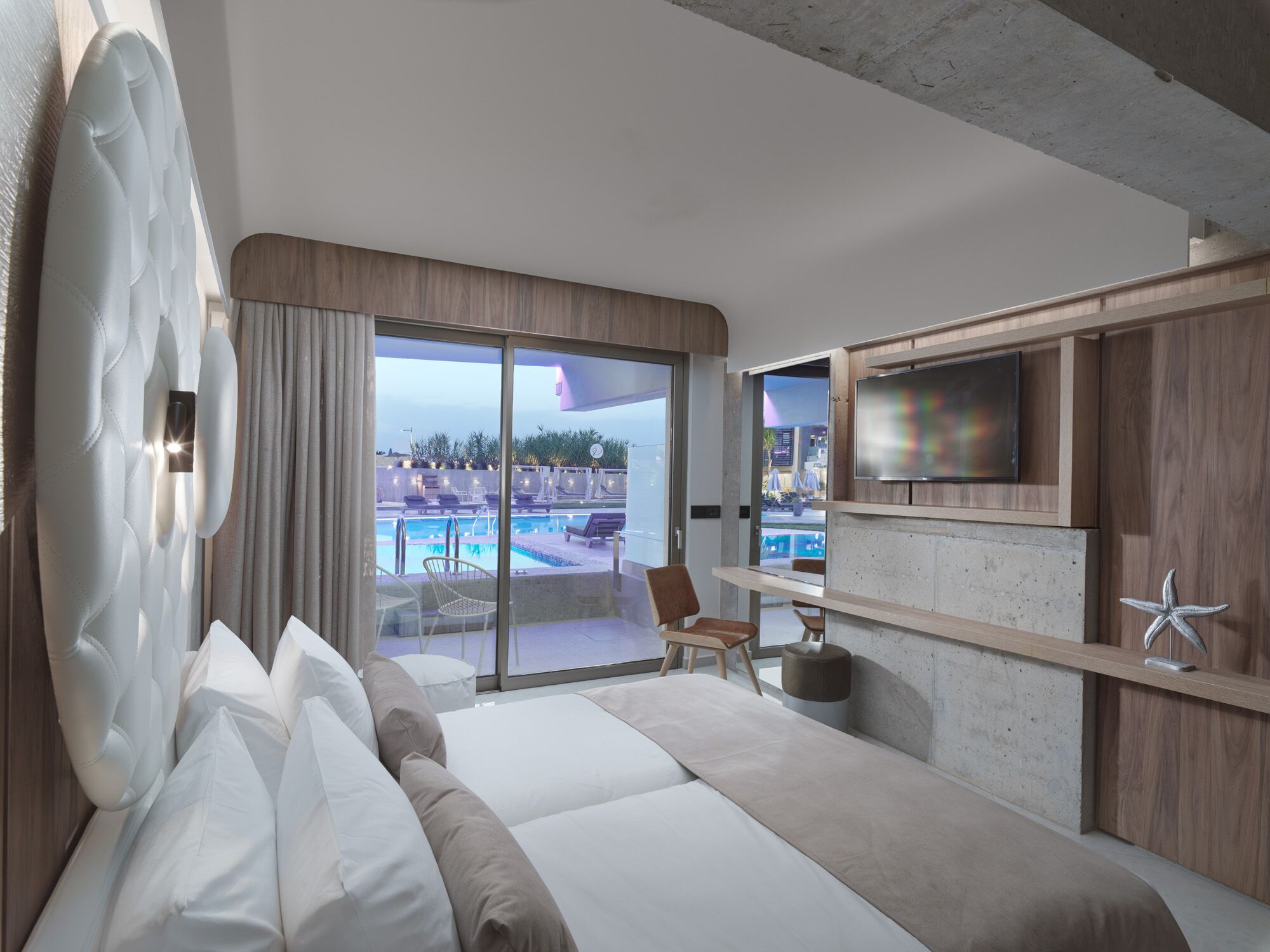Habitación de hotel moderna con una cama grande, televisor, escritorio y vista a una piscina.