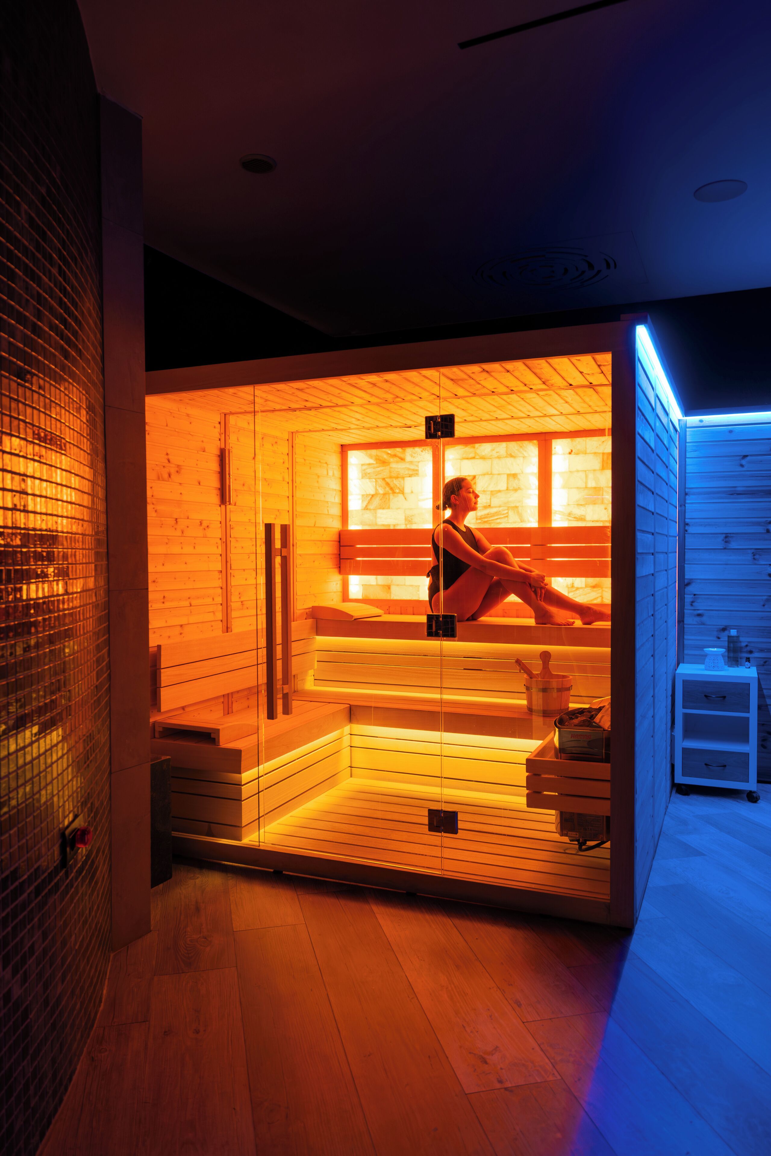 A sauna with a glass enclosure, wooden benches, and a wooden floor.