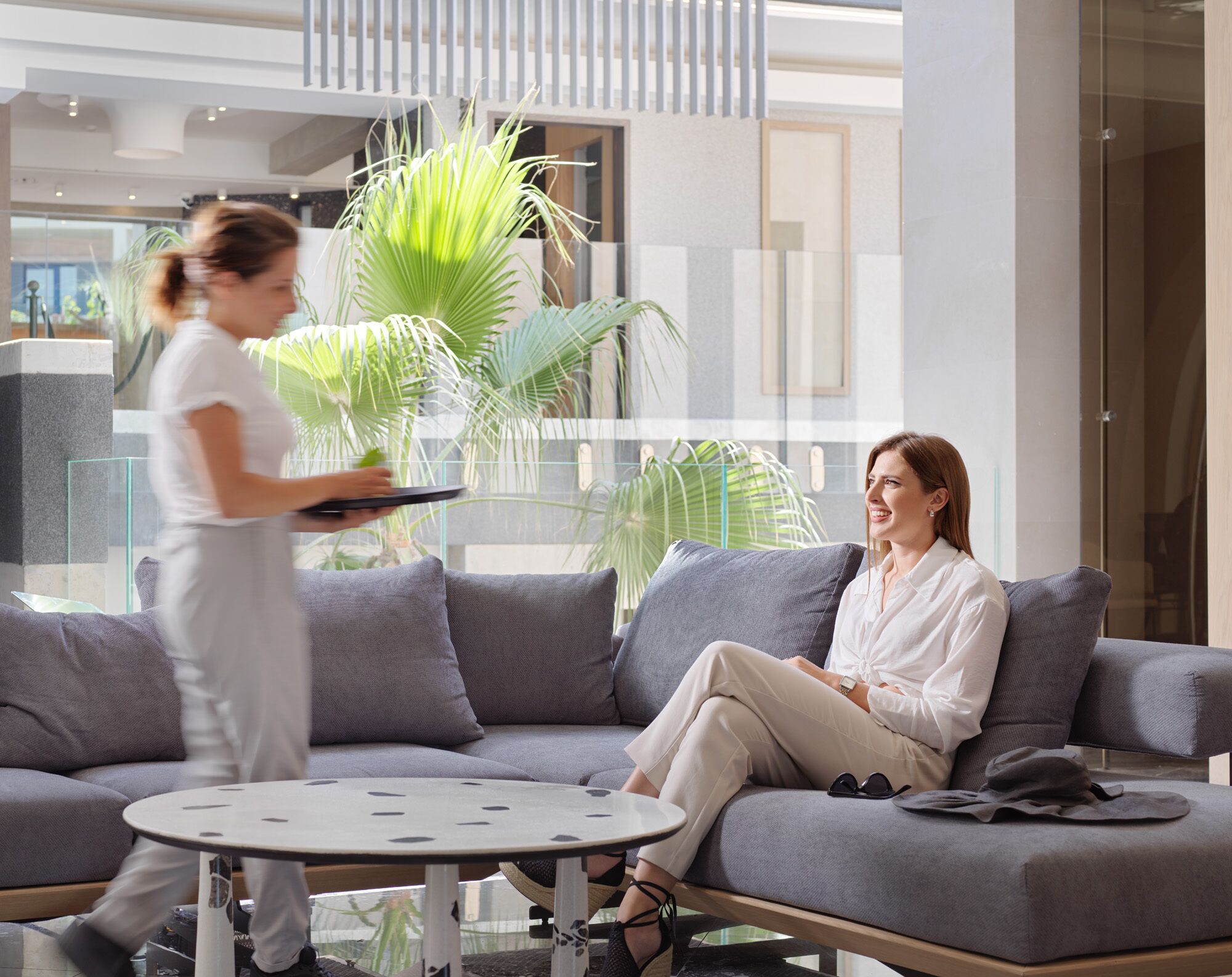 A modern lobby with a grey sofa, a round table, and a large potted plant.