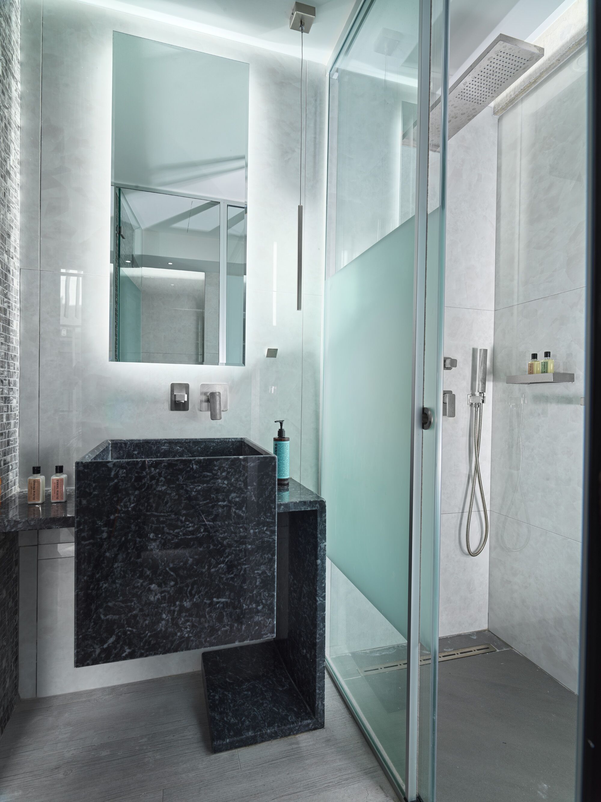 Un baño moderno con lavamanos de mármol, cabina de ducha de vidrio y un espejo grande.