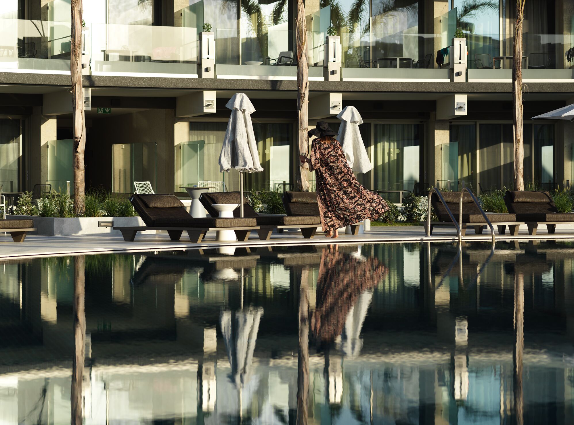 Un hotel moderno con piscina, sillas de descanso y una piscina reflectante.