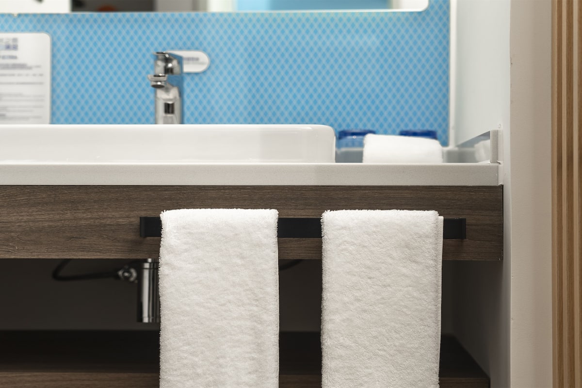 A bathroom with a white sink, a blue tiled wall, and two white towels hanging on a rack.