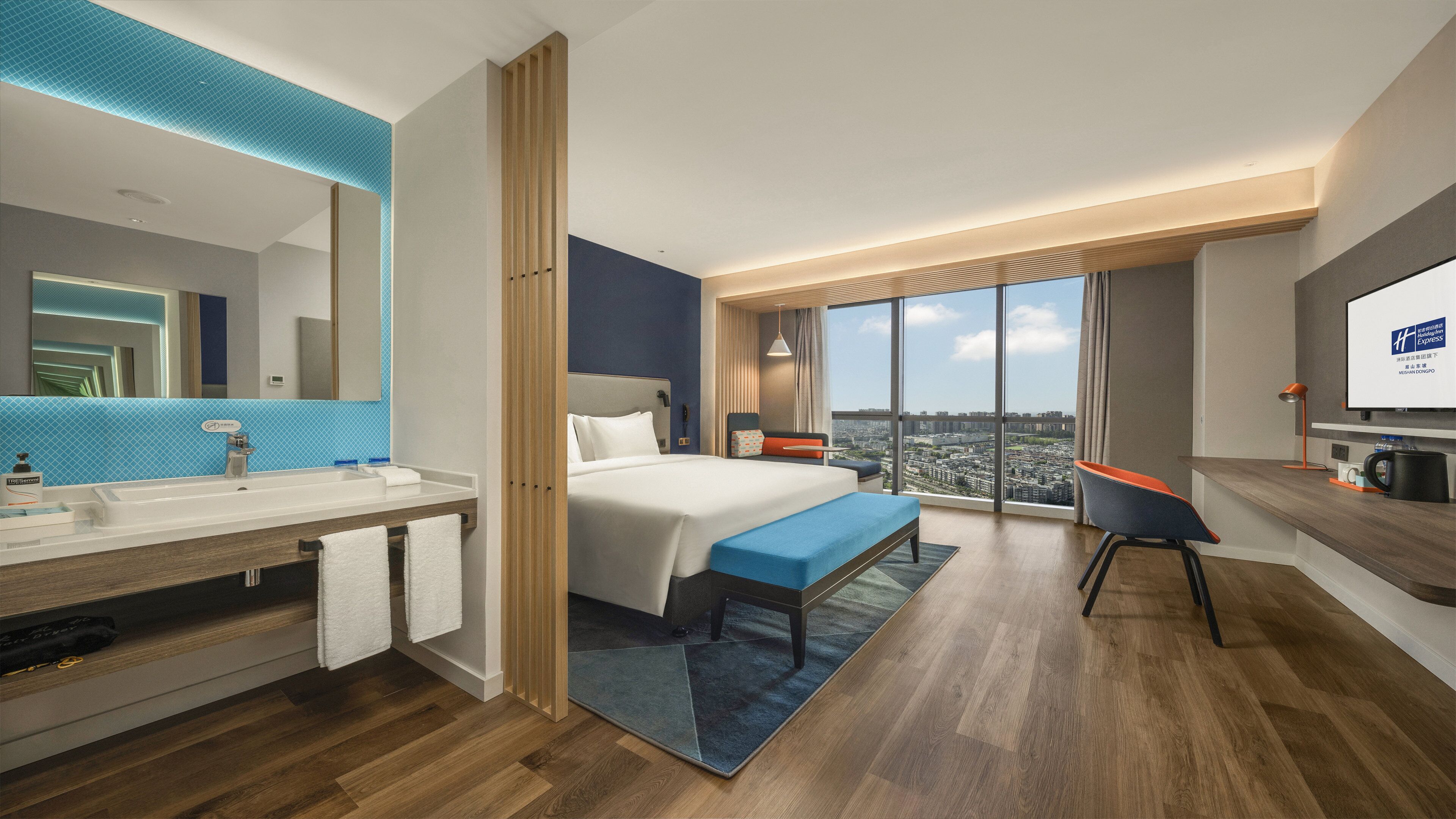 Et moderne hotelværelse med en stor seng, et skrivebord, et badeværelse med håndvask og spejl, samt udsigt over byen.