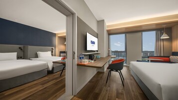 Habitación de hotel moderna con una cama grande, un escritorio con silla, un televisor y vistas a la ciudad.