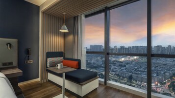 A modern room with a city view, a sofa, a table, a phone, and a lamp.