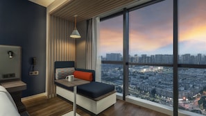 A modern room with a city view, a sofa, a table, a phone, and a lamp.