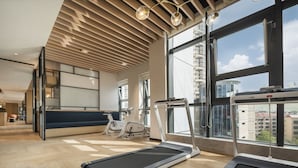 Une salle de sport moderne, dotée d’appareils d’exercice, de grandes fenêtres et d’un plafond haut avec des lambris en bois.