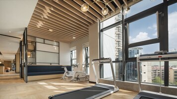 A modern gym with exercise equipment, large windows, and a high ceiling with wooden slats.