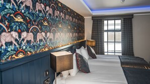 A hotel room with a large bed, a headboard with a patterned mural, a bedside table with a lamp, and a window with curtains.