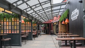 A covered outdoor dining area with tables and chairs, a sign for Monck's Lane, and a view of the street.