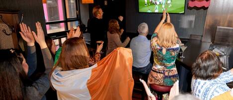A group of people watching a sports event on a television screen in a room with a bar area.