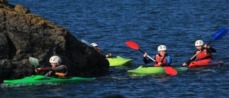 Tres kayakistas en kayaks verde y rojo remando cerca de una costa rocosa.
